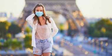 Paris 'teki Eyfel Kulesi' nin yanında duran ve Coronavirus salgını sırasında koruyucu maske takan genç bir kız. Fransa 'da salgın ve tecrit. Karantinadan sonra Fransa 'da tatil yapan turistler
