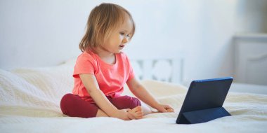 Evde dijital tableti olan küçük bir kız. Çocuk çizgi film izliyor. Çocuk arkadaşlarıyla ya da anaokulu öğrencileriyle iletişim kurmak için alet kullanıyor. Çocuklar için eğitim ve uzak mesafe eğitimi. Evde kalıp eğlenin.