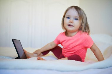 Evde dijital tableti olan küçük bir kız. Çocuk çizgi film izliyor. Çocuk arkadaşlarıyla ya da anaokulu öğrencileriyle iletişim kurmak için alet kullanıyor. Çocuklar için eğitim ve uzak mesafe eğitimi. Evde kalıp eğlenin.