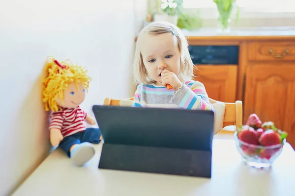 愛らしい幼児の女の子は新鮮なイチゴを食べ タブレットを使用しています 子供の漫画を食べながら見ている 子供の教育におけるデジタル技術 — ストック写真