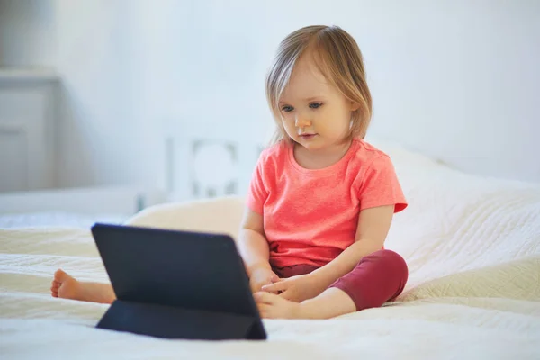 Toddler girl with digital tablet at home. Child watching cartoons. Kid using gadget to communicate with friends or kindergartners. Education and distance learning for kids. Stay at home entertainment