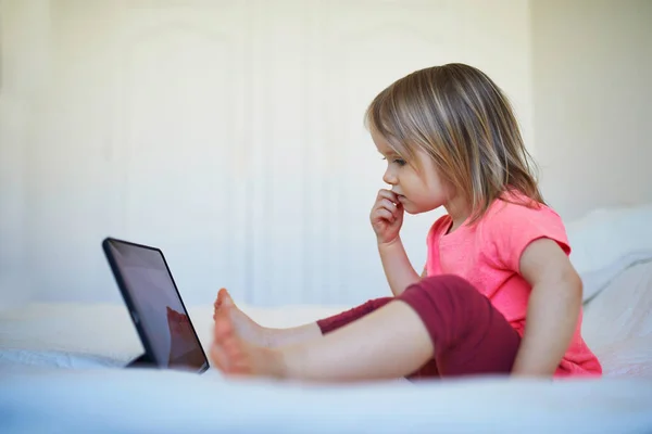Toddler girl with digital tablet at home. Child watching cartoons. Kid using gadget to communicate with friends or kindergartners. Education and distance learning for kids. Stay at home entertainment