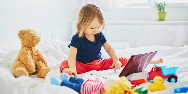 ベッドの中でラップトップとおもちゃと幼児の女の子 友達や幼稚園生とコミュニケーションするためにガジェットを使用して子供 子供と一緒に家から教育 距離学習や仕事 ホームエンターテイメントに滞在する — ストック写真