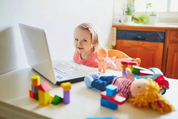 Happy toddler girl with laptop and toys. Kid using computer to communicate with friends, elderly relatives or kindergartners. Education or online communication for kids. Stay at home entertainment