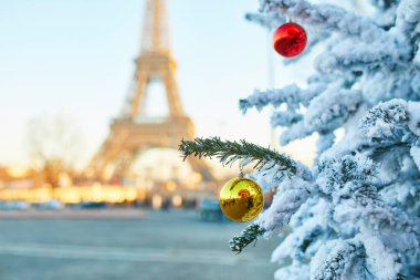 Karla kaplı ve kırmızı ve sarı toplarla süslenmiş Noel ağacı, arka planda Eyfel kulesi. Paris, Fransa 'da sezon tatilleri
