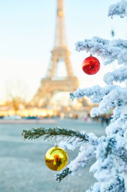 Karla kaplı ve kırmızı ve sarı toplarla süslenmiş Noel ağacı, arka planda Eyfel kulesi. Paris, Fransa 'da sezon tatilleri