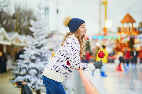 フランスのパリのクリスマスマーケットで幸せな若い女性 スケートリンクの近くに赤いカラメルアップルと女の子 クリスマスと新年の野外活動 — ストック写真