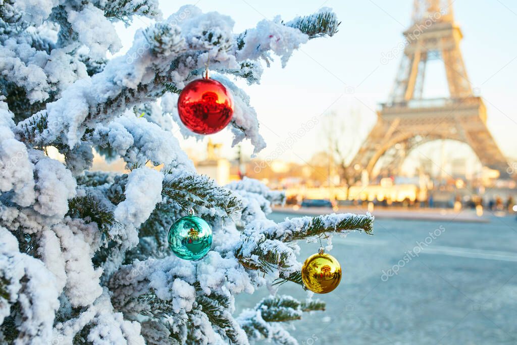 Christmas tree covered with snow and decorated with red, green and yellow balls, Eiffel tower in the background. Season holidays in Paris, France
