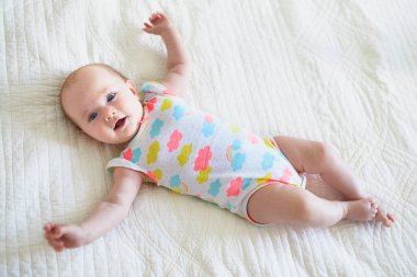 Sevimli, gülümseyen bir kız bebek bebek odasında yatakta yatıyor.