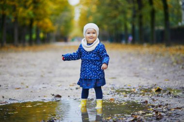 Sarı çizme giyen ve sonbahar günü su birikintisine atlayan bir çocuk. Tatlı küçük kız yağmurlu bir günde parkta su ve çamurla eğleniyor. Çocuklar için açık hava sonbahar aktiviteleri