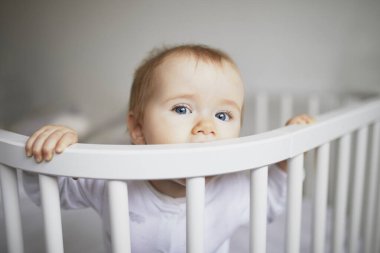 Ebeveyn yatağına bağlı, birlikte uyuyan sevimli bir kız bebek. Küçük çocuk karyolada oturuyor.