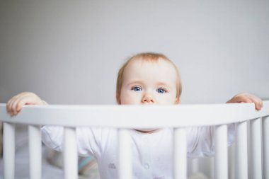 Ebeveyn yatağına bağlı, birlikte uyuyan sevimli bir kız bebek. Küçük çocuk karyolada oturuyor.