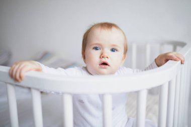 Ebeveyn yatağına bağlı, birlikte uyuyan sevimli bir kız bebek. Küçük çocuk karyolada oturuyor.