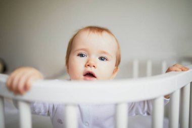 Ebeveyn yatağına bağlı, birlikte uyuyan sevimli bir kız bebek. Küçük çocuk karyolada oturuyor.