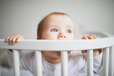 Ebeveyn yatağına bağlı, birlikte uyuyan sevimli bir kız bebek. Küçük çocuk karyolada oturuyor.