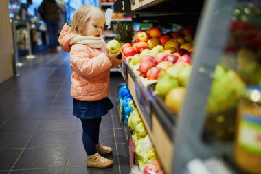 Süpermarkette elma toplayan sevimli bir kız bebek. Küçük çocuk alışverişe gidiyor. Geniş yiyecek ya da marketteki çocuk.