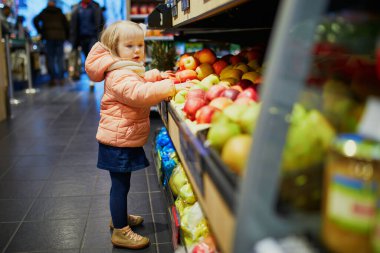 Süpermarkette elma toplayan sevimli bir kız bebek. Küçük çocuk alışverişe gidiyor. Geniş yiyecek ya da marketteki çocuk.