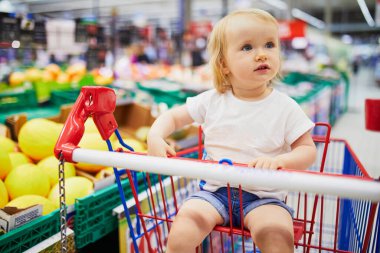 Markette ya da süpermarkette alışveriş arabasında oturan küçük tatlı bir kız. Küçük çocuk alışverişe gidiyor.