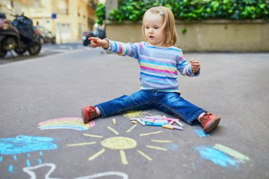 Asfalta renkli tebeşirler çizen sevimli küçük kız. Küçük çocuklar için açık hava aktiviteleri ve yaratıcı oyunlar