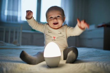 Bebek odasında başucunda lambayla oynayan sevimli bir kız. Gece lambasıyla yatakta oturan mutlu çocuk. Küçük çocuk uyumadan önce akşam evde.
