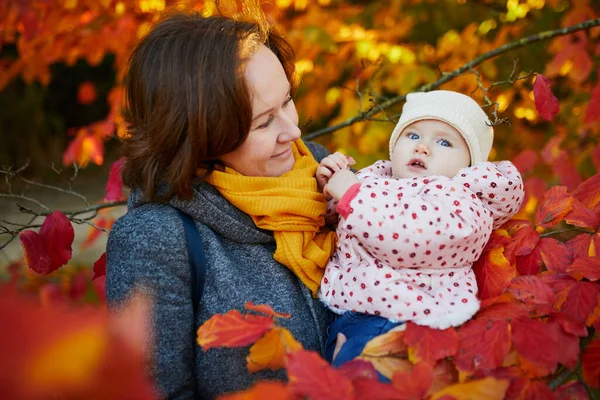 公園で晴れた秋の日に赤ちゃんの女の子と幸せな笑顔の女性 2つの明るい赤い葉の美しい家族 子供と一緒に秋の活動 — ストック写真