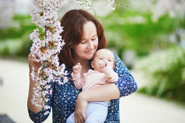 小さな女の子を屋外で抱えている幸せな若い女性 母は春の日に娘と一緒に歩く 桜の季節を楽しむ親子 — ストック写真