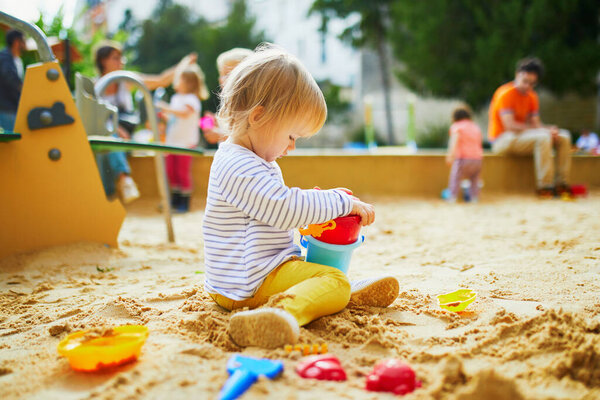 Adorable little girl on playground in sandpit. Toddler playing with sand molds and making mudpies. Outdoor creative activities for kids