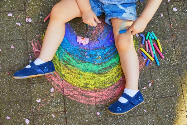 蹒跚学步的女孩用彩色粉笔在沥青上画彩虹 孩子画她的腿很开心 幼儿户外活动及创意游戏 — 图库照片