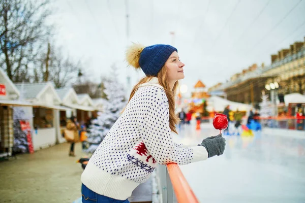 フランスのパリのクリスマスマーケットで幸せな若い女性 スケートリンクの近くに赤いカラメルアップルと女の子 クリスマスと新年の野外活動 — ストック写真