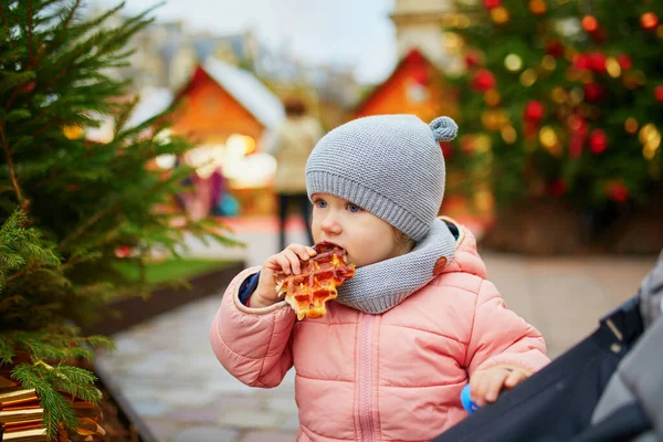 パリのクリスマスマーケットでワッフルを食べる愛らしい幼児の女の子 季節の休暇中に屋外で楽しい時間を過ごす幸せな子供 クリスマスと新年を子供たちと祝う — ストック写真