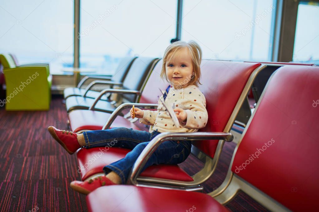 Adorable little toddler girl traveling by plane. Child sitting in gate and waiting for the flight. Traveling abroad with kids. Unaccompanied minor concept