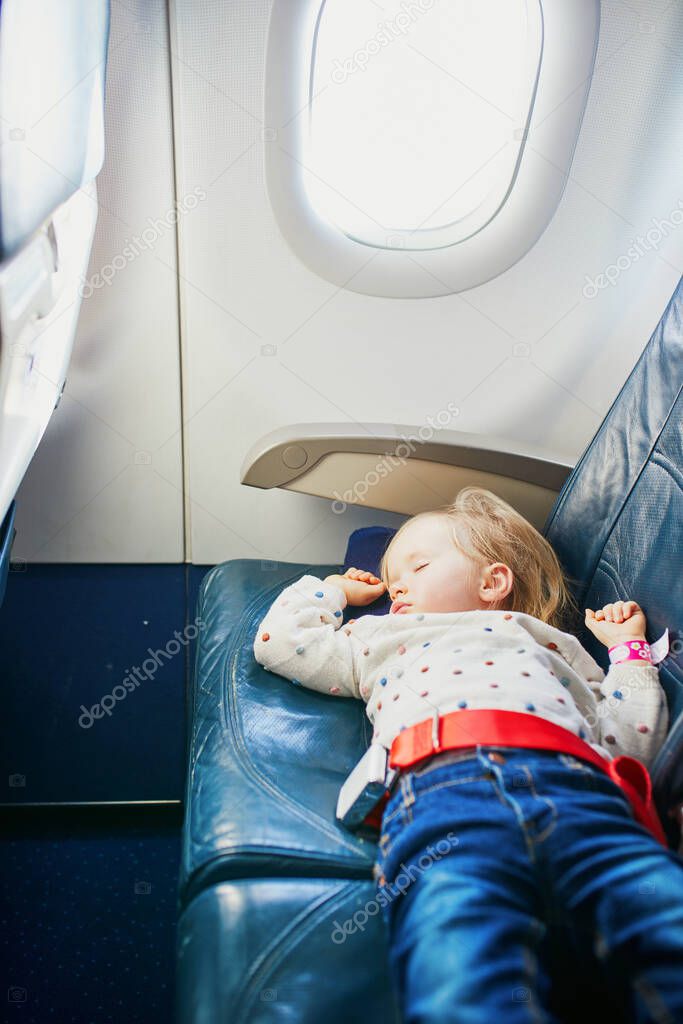 Adorable little toddler girl traveling by plane. Small child lying on a seat and sleeping during the flight. Traveling abroad with kids. Unaccompanied minor concept