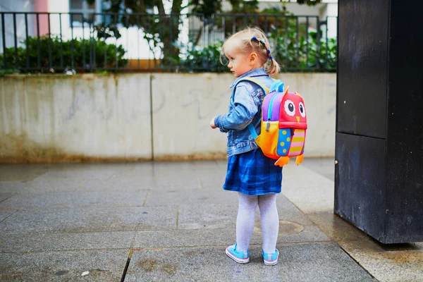 Adorable toddler girl with funny backpack ready to go to daycare, kindergarten or school. First day of school concept