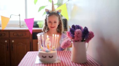 Altıncı yaş gününü kutlayan, mumları üfleyen ve dilek tutan tek boynuzlu at saçlı mutlu küçük kız.