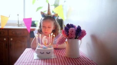 Altıncı yaş gününü kutlayan, mumları üfleyen ve dilek tutan tek boynuzlu at saçlı mutlu küçük kız.