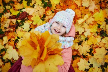 Fransa, Paris 'teki sonbahar parkında düşmüş akçaağaç yapraklarıyla kaplı yerde yatan mutlu küçük kız.