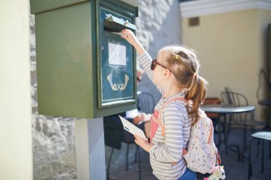 Sevimli anaokulu kızı Estonya 'nın Tallinn caddesinde bir posta kutusuna kartpostal atıyor.
