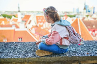 Sırt çantalı sevimli anaokulu kızı Estonya 'nın Tallinn şehrinin eski manzarasının tadını çıkarıyor.