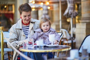 Güzel genç anne ve tatlı küçük kızı Paris, Fransa 'daki açık kafede eğleniyorlar.