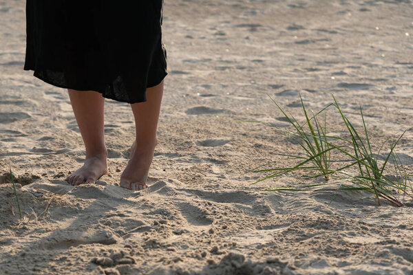 Женщина в юбке и с голыми ногами на песке у Балтийского моря.