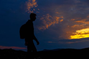 Sırt çantalı yürüyüşçü siluetleri dağın tepesinden gün batımının tadını çıkarıyor. Kazanan siluet dağın tepesinde. Spor ve aktif yaşam konsepti