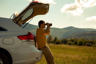 Young Man use of the binocular at forest. Tourist Camping on a car clipart