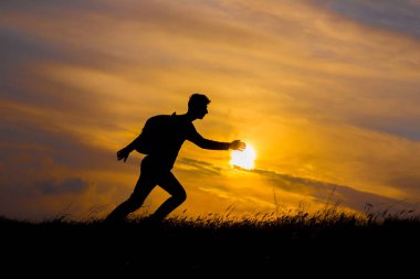 Hayallerinin peşinden git, gün batımında insan silueti. Sırt çantalı bir yürüyüşçü sahada yürüyor. Gün batımında Yaz sağlıklı aktif yaşam tarzı. Tek yolculuk..