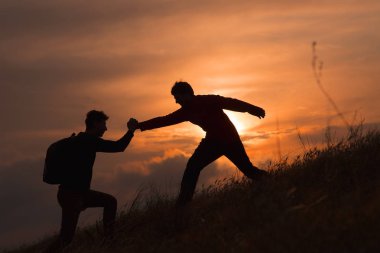 Yürüyüş yapan çift, dağlarda, gün batımında birbirlerine güven duymalarına yardımcı olur. Dağcılık takımının tepesinde birbirine yardım eden iki kişilik bir takım çalışması, güzel bir gün batımı manzarası.