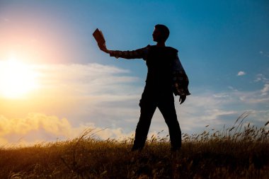 Parkta kitap okuyan adam. Akşamları denizin kenarında dalgakıran üzerinde oturan bir adamın silueti, kitap okuyor.
