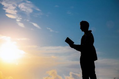 Parkta kitap okuyan adam. Akşamları denizin kenarında dalgakıran üzerinde oturan bir adamın silueti, kitap okuyor.