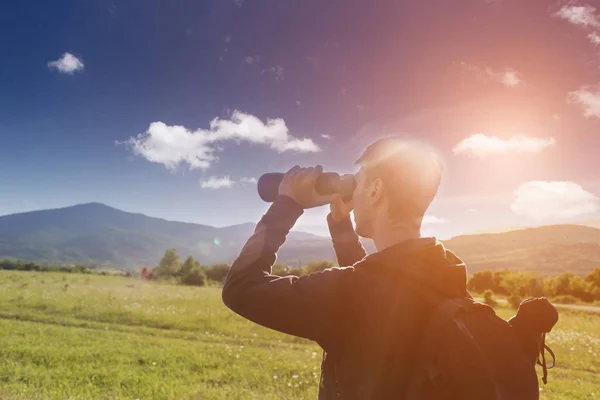 The side profile of Man watching though binoculars. Beautiful mountains landscape with clouds and with tourist binoculars.