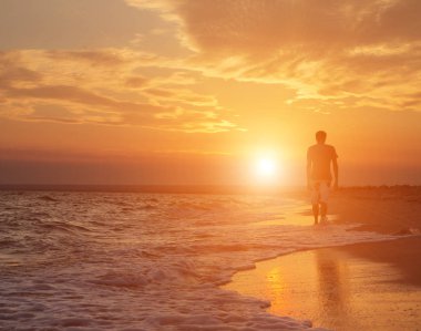 güzel bir gün batımı zemin karşı sahilde yürüyen genç bir adam silüeti