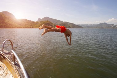 Sıcak bir yaz gününde teknesinin karşısındaki çocuk. Yatından okyanus mavisinde ferahlatıcı bir banyosu olan bir adam. Kostümlü çocuk denize daldı..