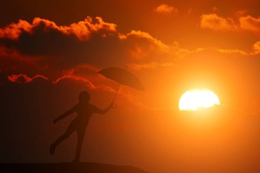 Gün batımında şemsiyeyle atlayan bir kızın silueti.